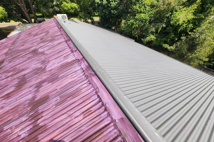 IBR metal roof mid-repaint showing Purple Prime rust-inhibiting primer beside the finished grey topcoat